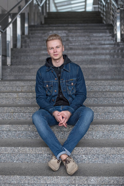 fellow is sitting on stairs in jeans and jeans jacket - Photo, Image
