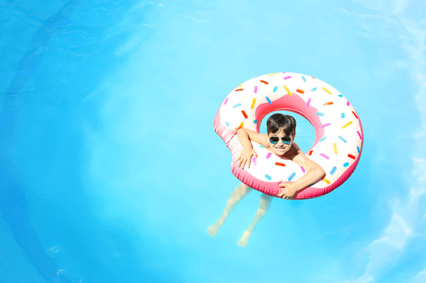 Cute little boy with inflatable donut in swimming pool - Foto, Imagen