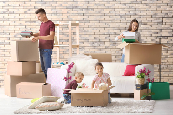 Happy family unpacking cardboard boxes in room at new house - Фото, изображение