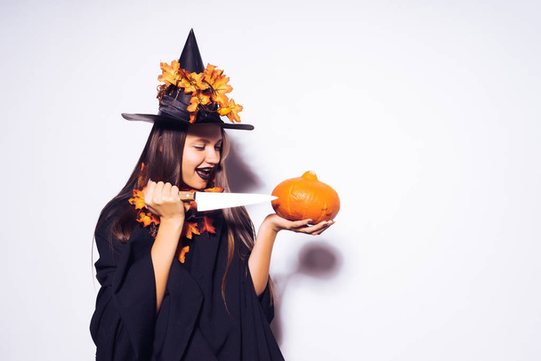 joyful girl in a suit of a witch prepares to cut a pumpkin - Photo, Image