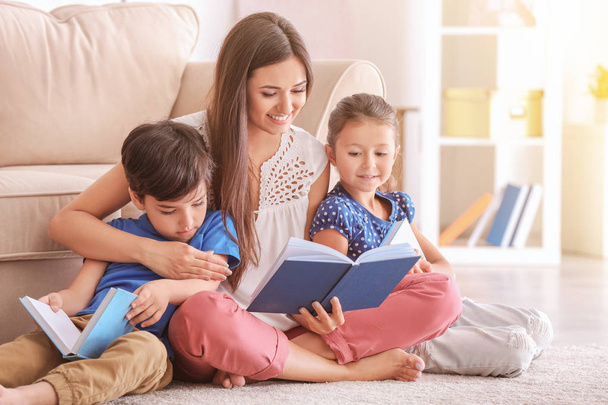 Young woman and her little children reading books at home - Foto, imagen