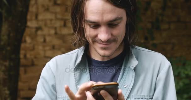 Millennial man in his 20s or 30s using one hand to type on smart phone - Video, Çekim