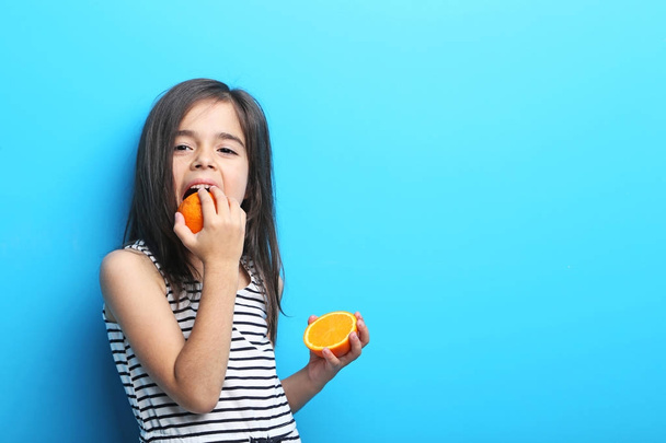Beautiful little girl with orange on blue background - Zdjęcie, obraz