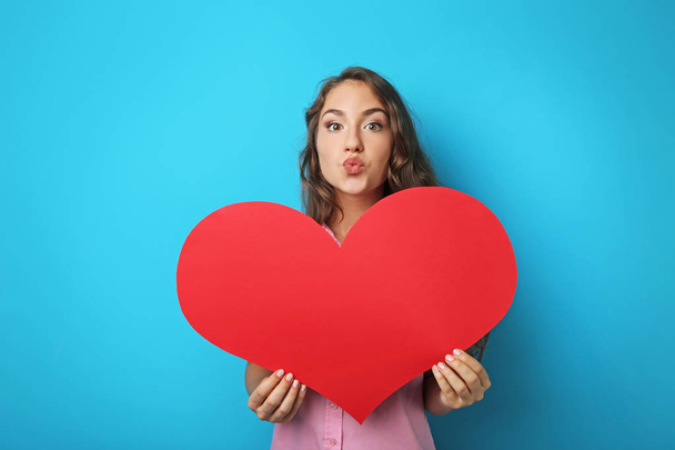 Portrait of young woman holding red heart on blue background - Foto, imagen