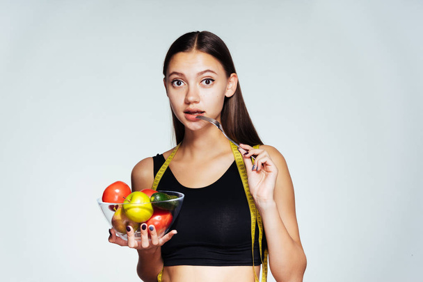 the girl looks thoughtfully forward holding a bowl of vegetables and apple in hands - Photo, Image