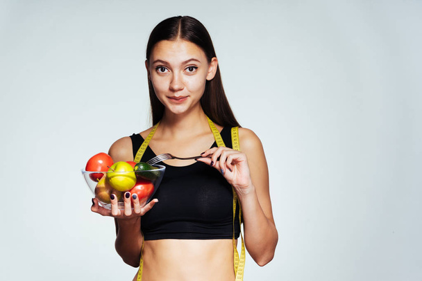 the girl joyfully looks forward holding a bowl of vegetables and an apple in hands - Fotó, kép