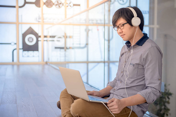 Jovem asiático trabalhando com laptop enquanto ouve música
 - Foto, Imagem
