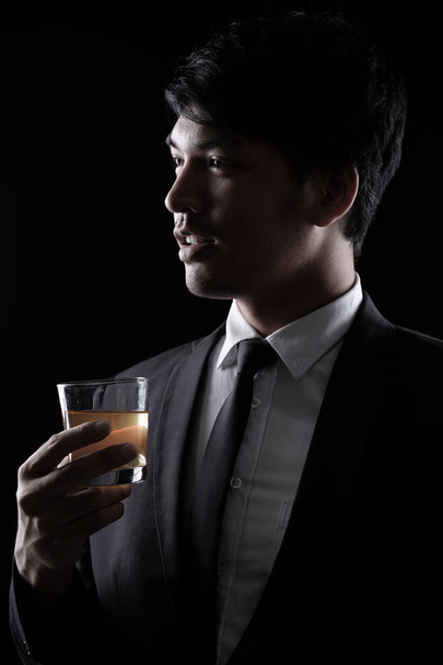 portret azjatycki człowiek w czarnym garniturze formalne z kieliszkiem wódki - Zdjęcie, obraz