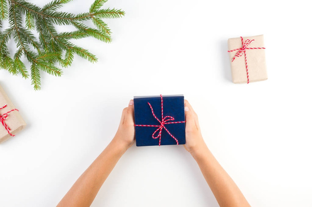 Vue du dessus des mains d'enfant tenant un cadeau. Coffrets cadeaux emballés dans du papier artisanal et branche d'arbre de Noël sur fond blanc
 - Photo, image