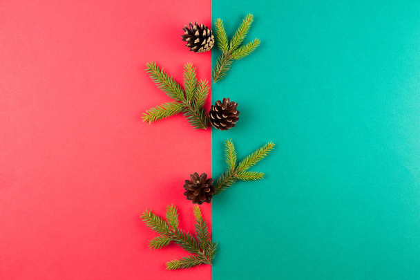 Composición navideña. Ramas de abeto y conos de pino dispuestos sobre fondo rojo y verde. Vista superior, plano
. - Foto, imagen