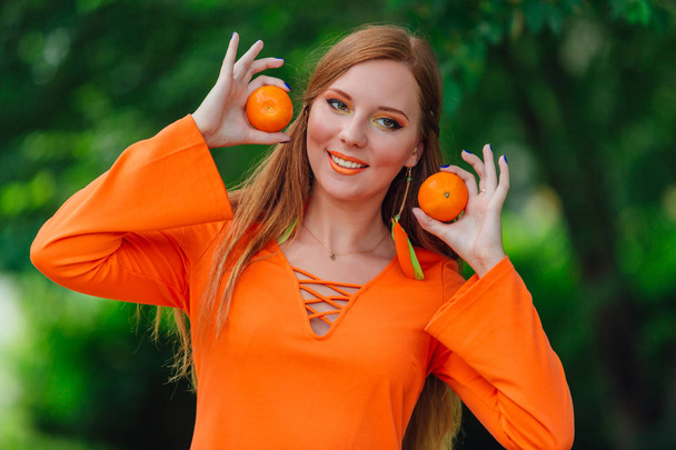 Portrait of pretty red hair woman with juicy delicious mandarins at summer green park. - Фото, изображение
