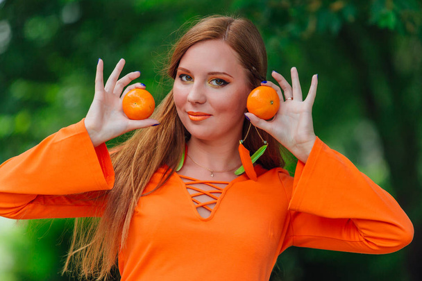 Portrait of pretty red hair woman with juicy delicious mandarins at summer green park. - Foto, Imagem