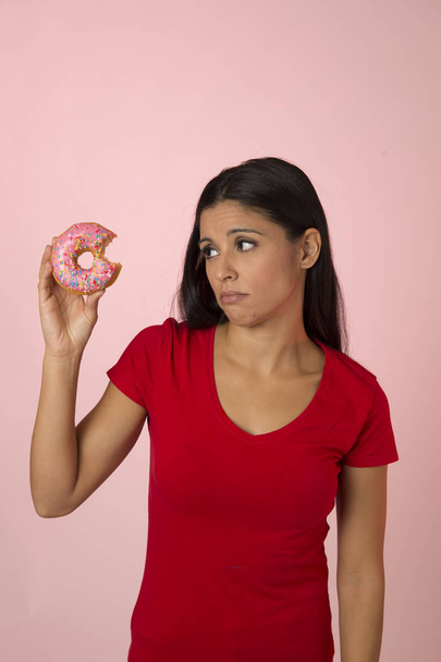 молодая красивая латинская женщина в красном с розовым сахарным пончиком думает и чувствует себя виноватой после укуса изолированы
 - Фото, изображение