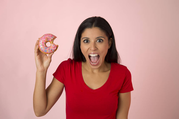 jovem mulher latina atraente feliz no topo vermelho sorrindo animado segurando donut açúcar isolado no fundo rosa
 - Foto, Imagem