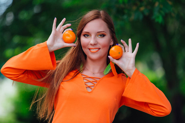 Portrait of pretty red hair woman with juicy delicious mandarins at summer green park. - Fotó, kép