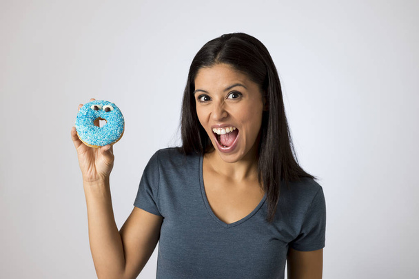 Gelukkig aantrekkelijke Latijnse vrouw die lacht enthousiast bedrijf suiker donut geïsoleerd op duidelijke achtergrond in suiker misbruik - Foto, afbeelding