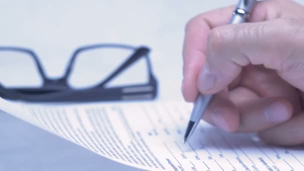 Male hand is writing in business document lying on the table. Close-up. - Video, Çekim