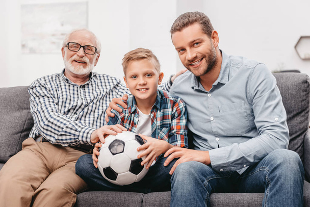 Família sentada no sofá com bola de futebol
 - Foto, Imagem