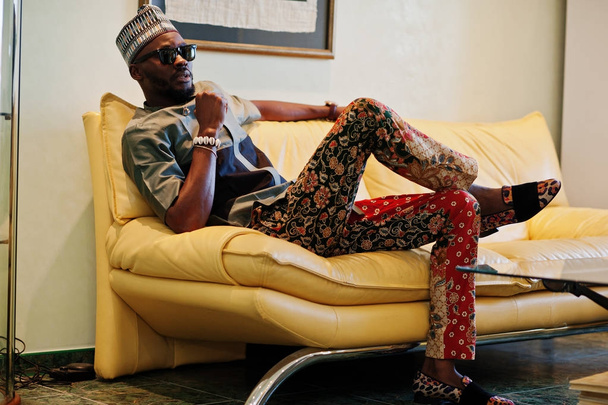Rich african man sitting on sofa at his appartment. Portrait of  - 写真・画像