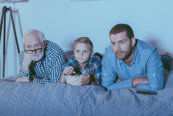Family with popcorn watching movie on bed - Photo, Image