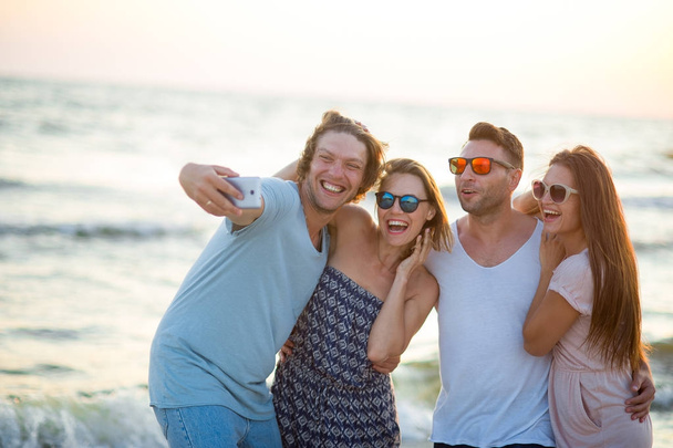 Groep van vrolijke jonge mensen gefotografeerd op het strand. - Foto, afbeelding