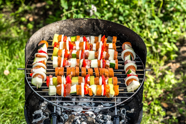 Шашлики на грилі на барбекю на траві, шампури з м'ясом та овочами, страви на грилі, відкритий барбекю в літньому саду
 - Фото, зображення