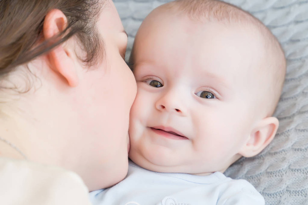 Close-up portrait of happy young mother hugging and kissing his sweet adorable child. Indoors shot, concept image - Zdjęcie, obraz
