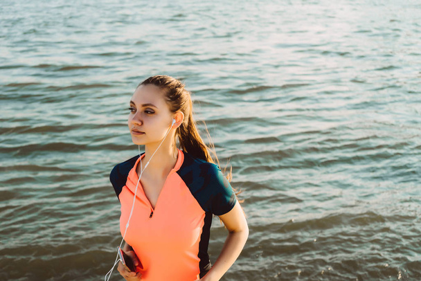 girl in a jogging track listening to music by the river - Φωτογραφία, εικόνα