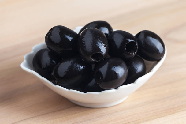 Bílá miska s černými olivami na dřevěný stůl - Fotografie, Obrázek