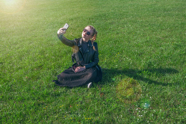 Красива блондинка сидить на зеленому газоні і робить селфі
 - Фото, зображення