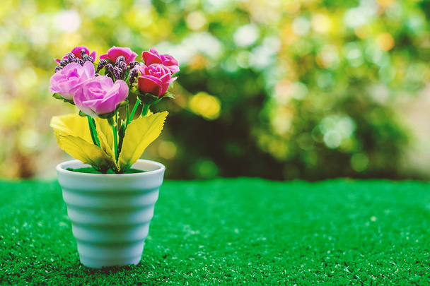 Artificial flower in flowerpot on green grass with blurred natural background - Photo, Image