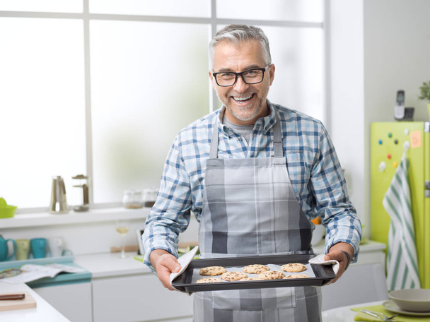 Sorrindo homem segurando biscoitos recém-assados
 - Foto, Imagem