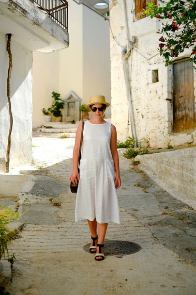 Young beautiful girl in straw hat walks through the narrow streets - Φωτογραφία, εικόνα