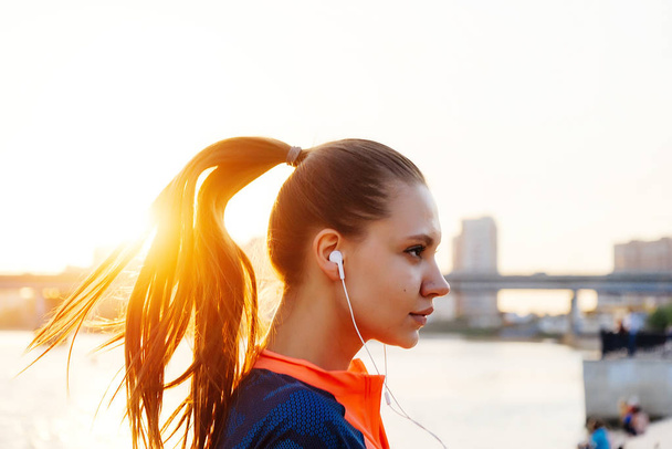 young sport girl jogging, in the evening by the river, listening to music on headphones - Photo, Image