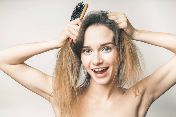 young funny girl having fun, trying to comb her fair-haired hair with a wooden comb - Photo, image