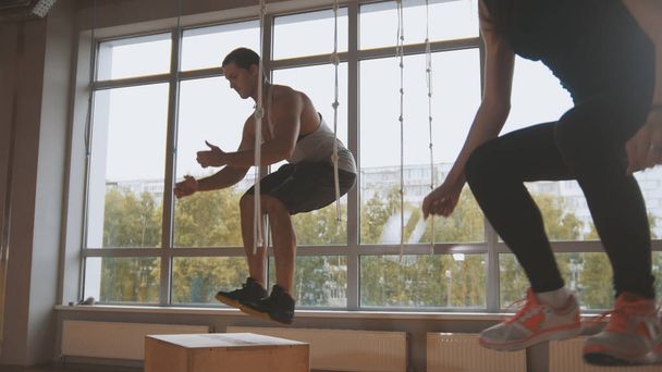 Jovem atraente menina e musculoso homem instrutor de fitness fazendo caixa de salto exercício durante um treino no ginásio
 - Foto, Imagem