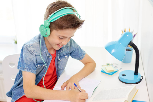 student boy in headphones writing to notebook - Foto, Imagen