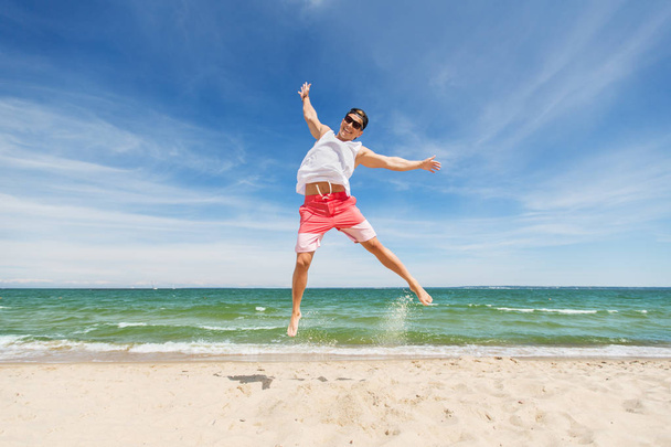усміхнений молодий чоловік стрибає на літньому пляжі
 - Фото, зображення
