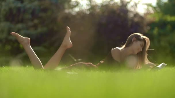 Mladá žena leží v trávě a čte knihu zpomalené - Záběry, video