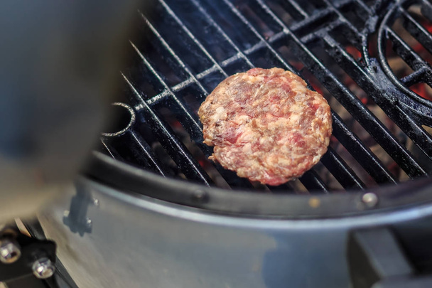 Raw beef hamburger begins roast on a barbecue grid - Photo, Image