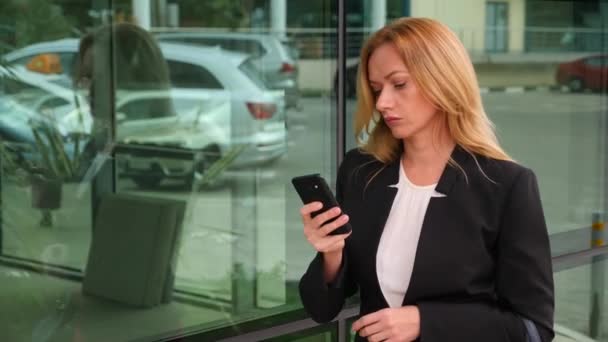 business woman in a business suit with a smartphone, walking on a business center, walking in the city, steadicam shot. 4k, slow motion, copy space - Video, Çekim