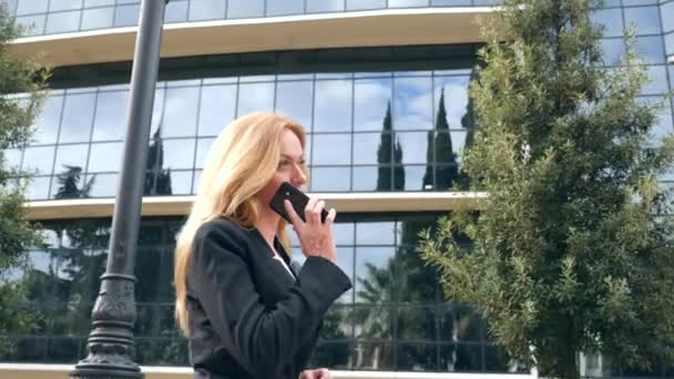 business woman in a business suit with a smartphone, walking on a business center, walking in the city, steadicam shot. 4k, slow motion, copy space - Felvétel, videó