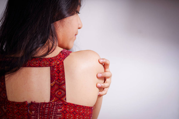 Close up of a young woman scratching her shoulder with her hand after being raped and suffering sexual abuse, in a white background - Foto, afbeelding