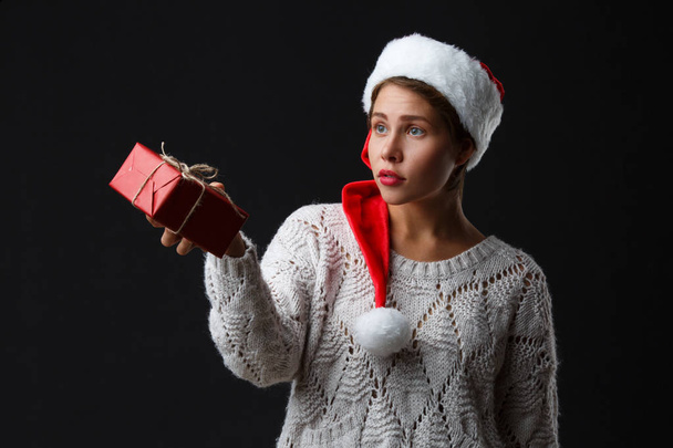 A girl in a santa hat holds a gift on a black background. - Fotó, kép