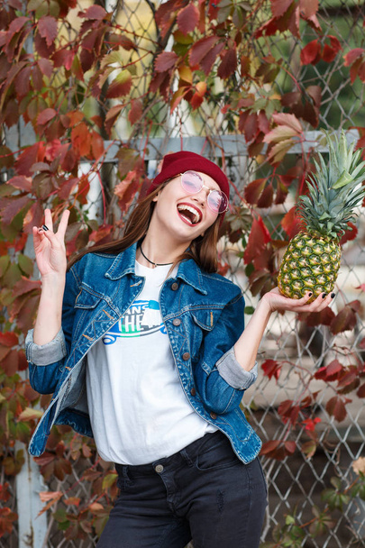 A girl with a pineapple is standing on the street on an autumn background - Photo, image