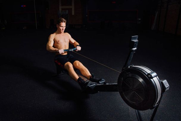 Fitness young man using rowing machine in the gym - Valokuva, kuva