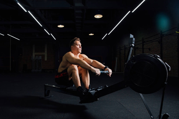 Fitness young man using rowing machine in the gym - Photo, image