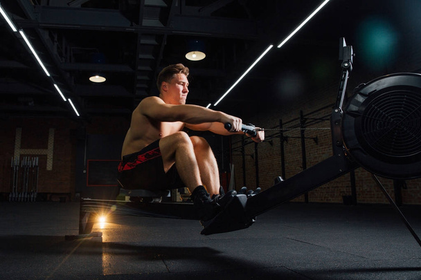 Fitness young man using rowing machine in the gym - 写真・画像