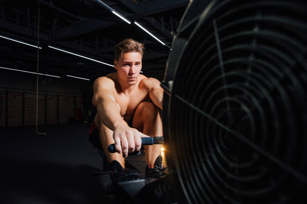 Fitness young man using rowing machine in the gym - Foto, immagini