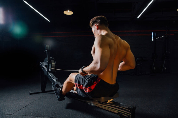 Fitness jeune homme utilisant la machine à ramer dans la salle de gym
 - Photo, image